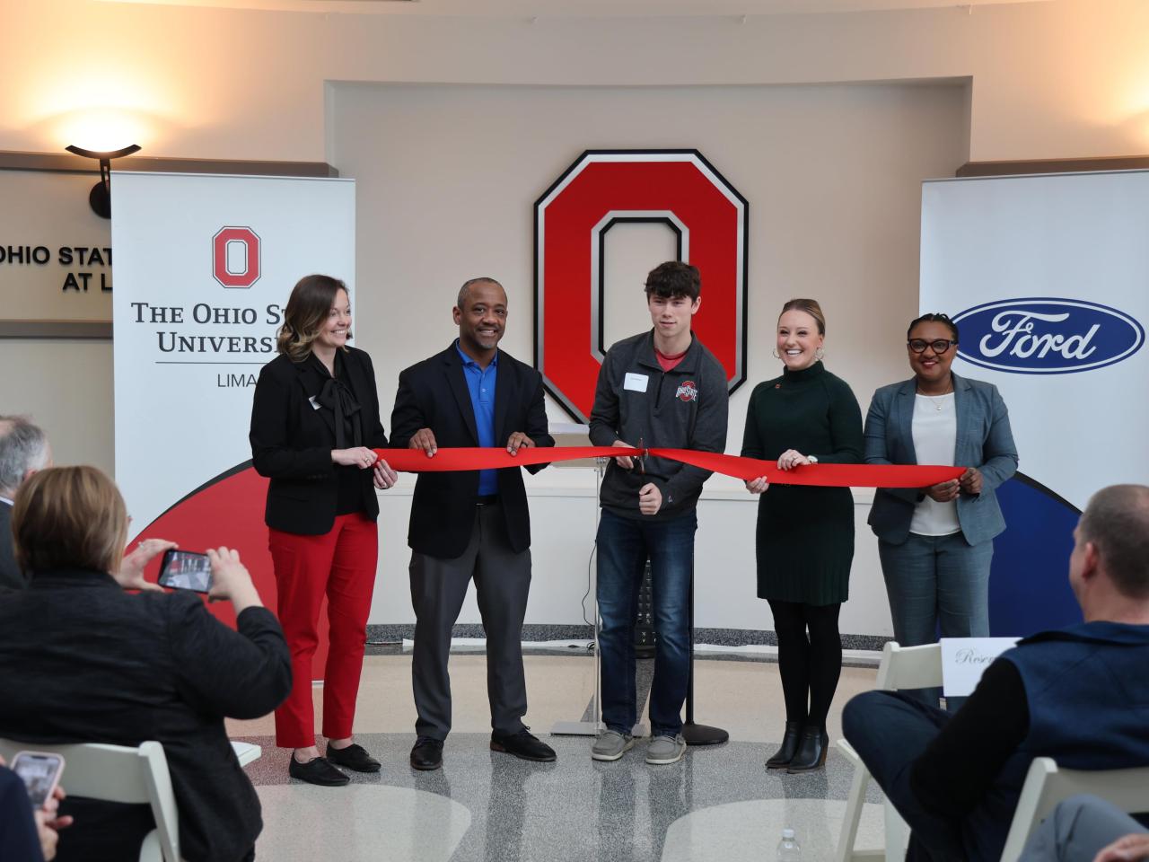 Five people cut a ribbon in front of a Block O 