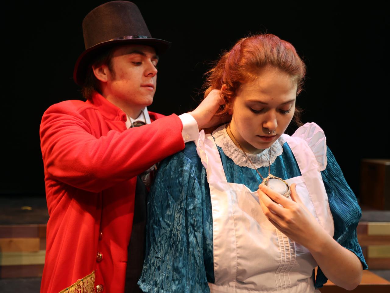A man in a top hat and red coat puts an amulet around a woman's neck