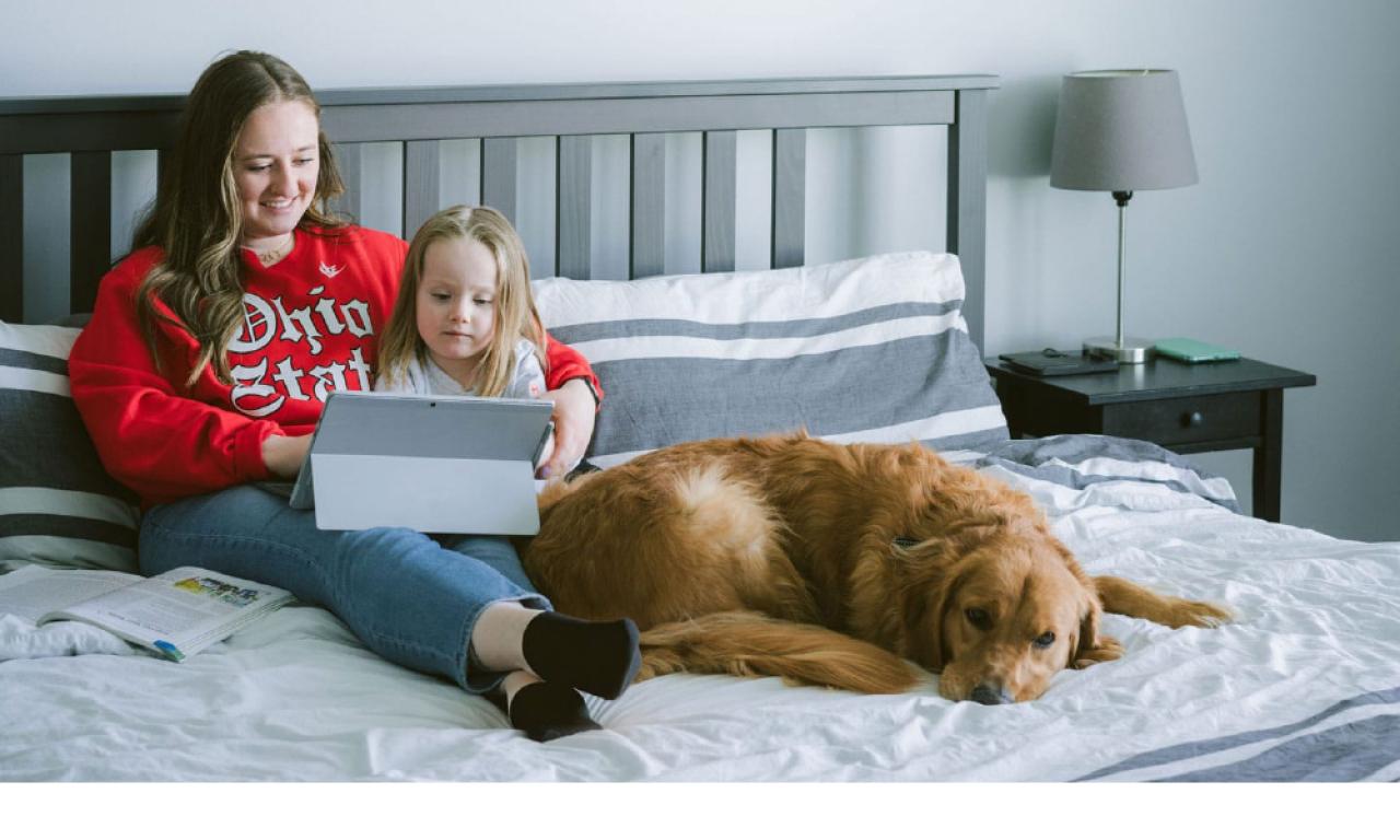 A student and a child look at a tablet next to a dog