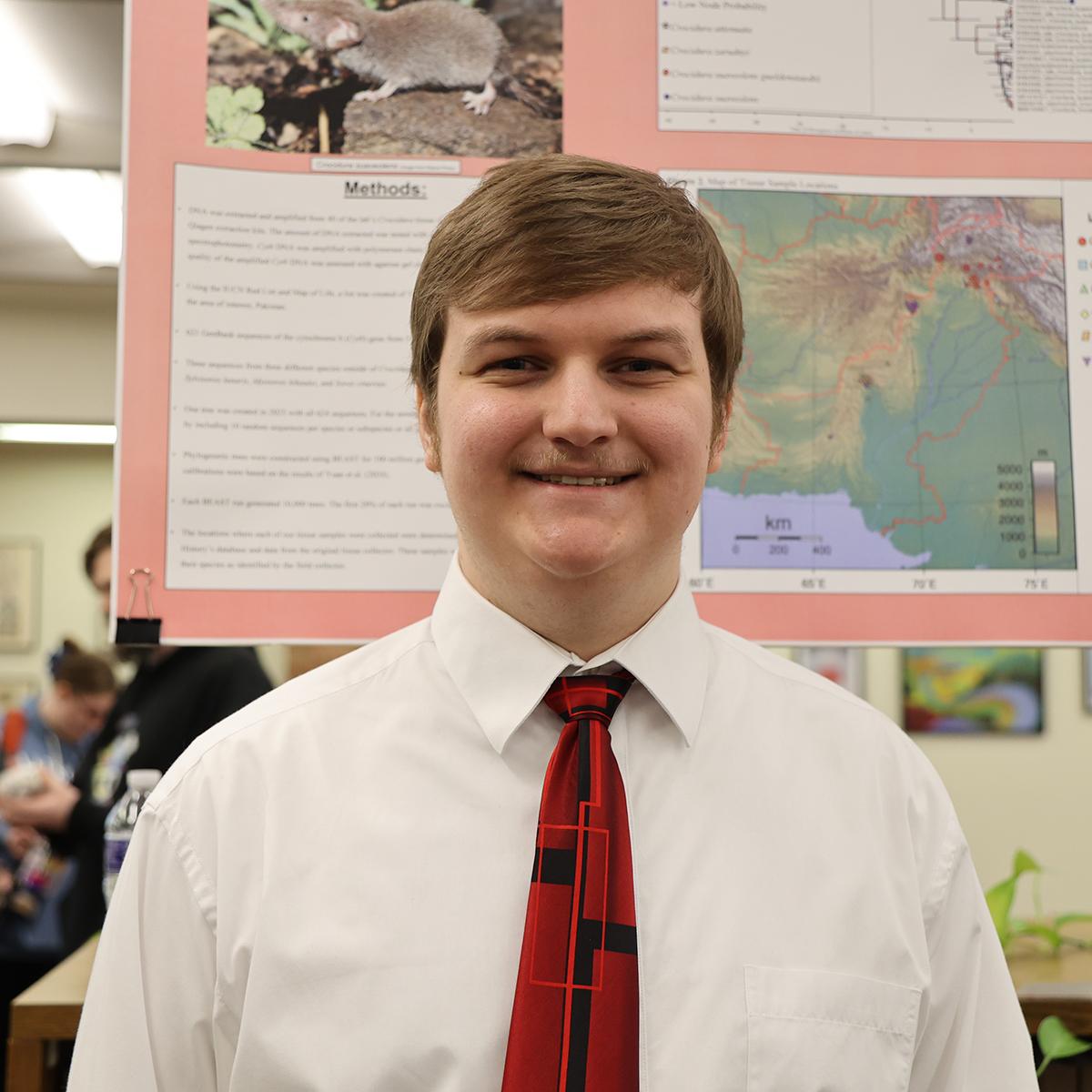 A student stands in front of his research poster