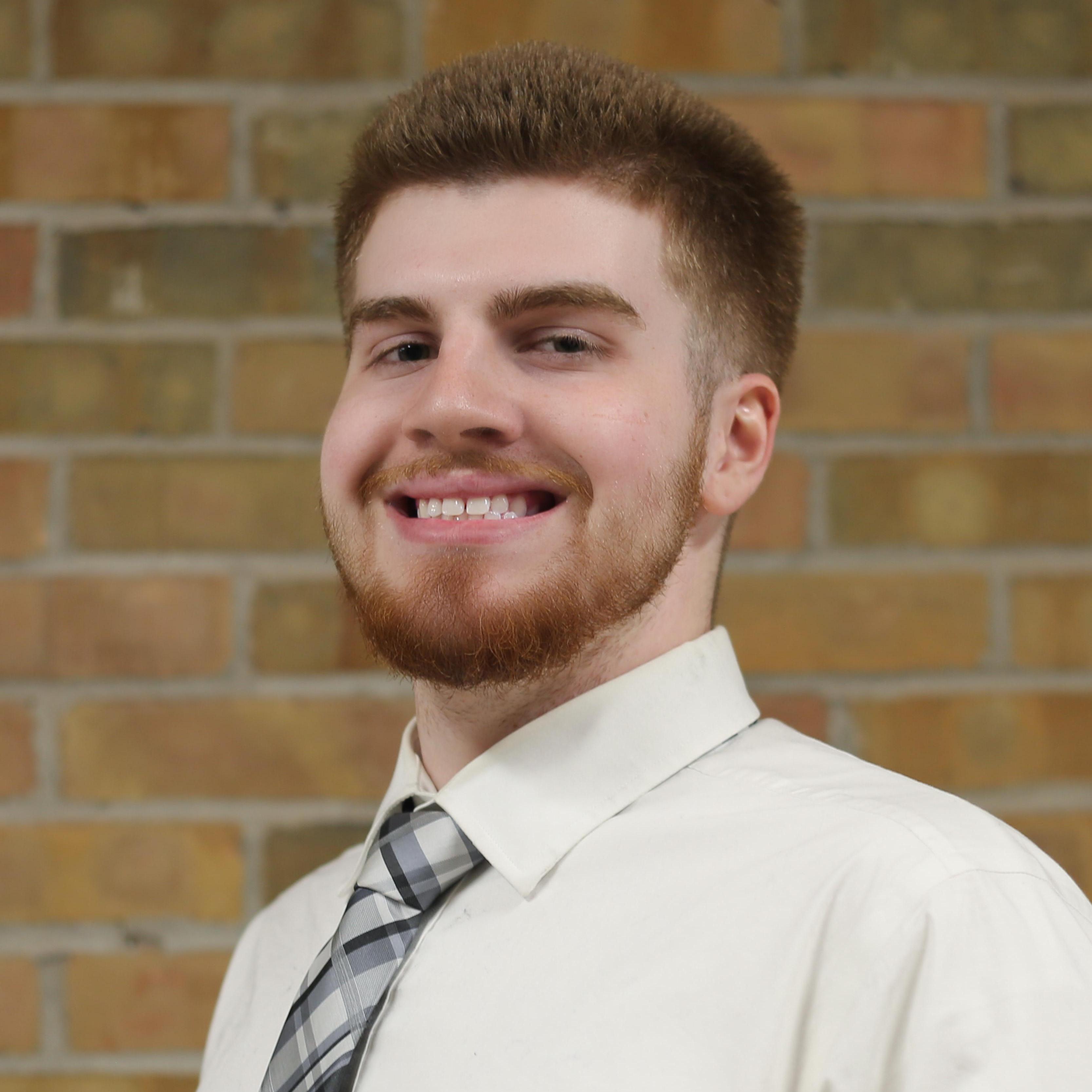 A student in a tie smiles in front of a brick wall