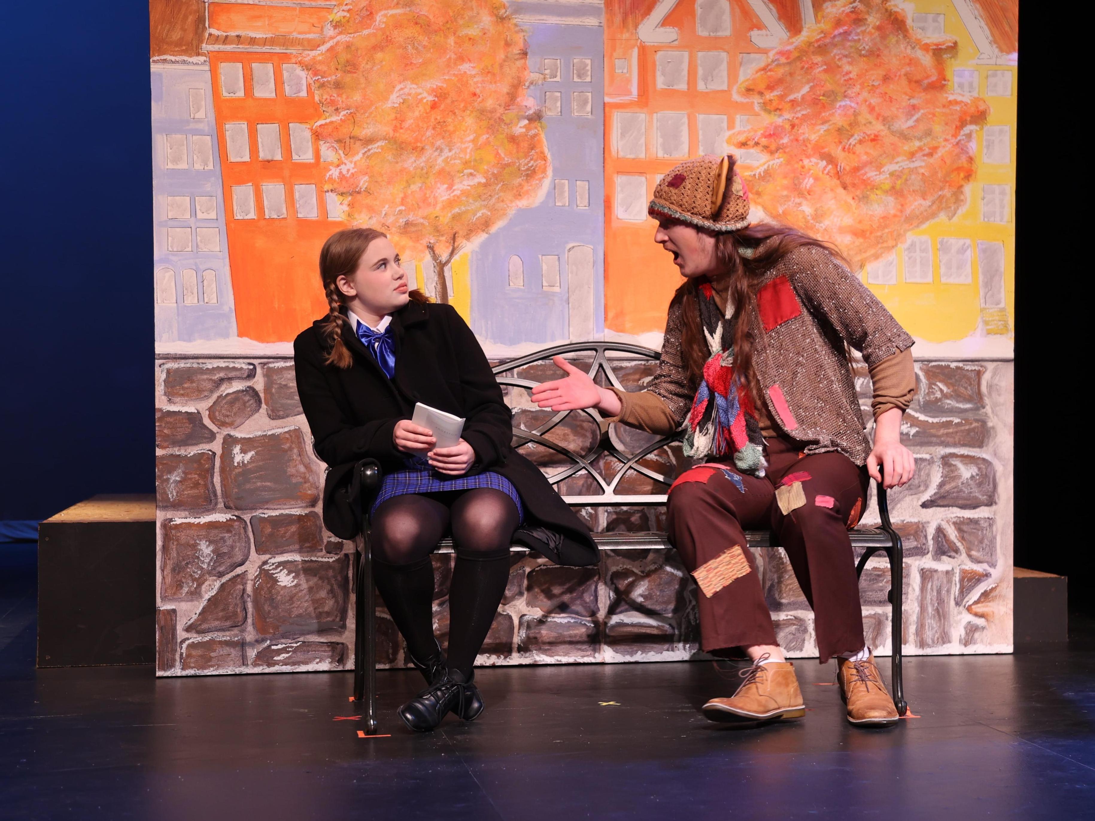 A girl on a bench leans away from a man dressed as a troll.