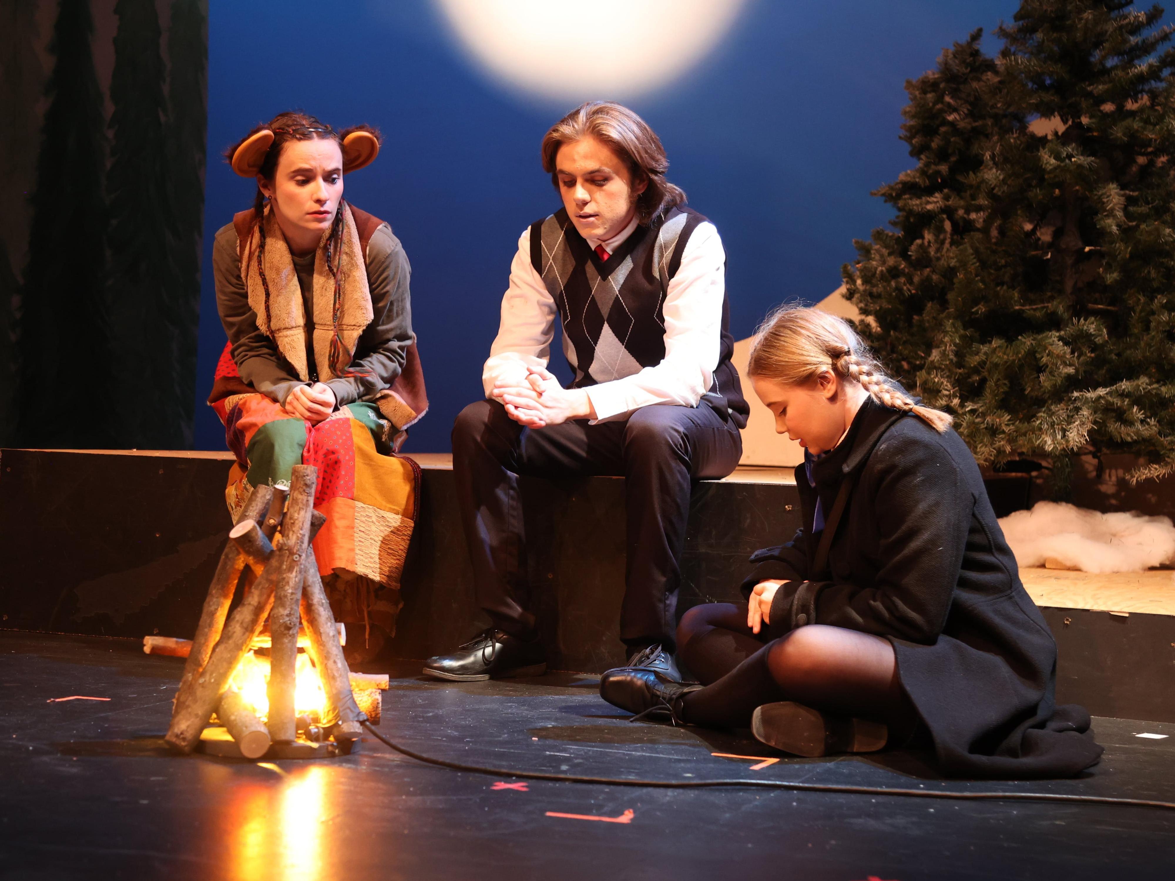 Three people sit around a campfire on stage at Ohio State Lima