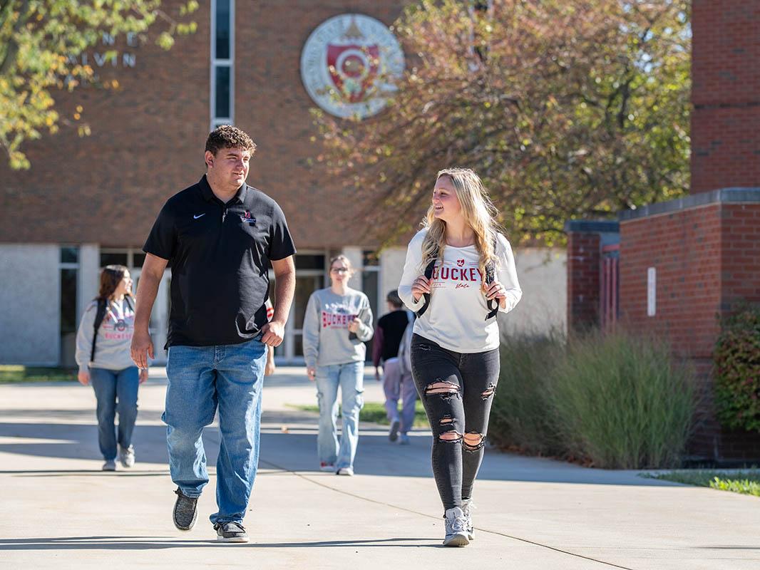 Two students walk on a campus sidewalk with Galvin Hall in the background
