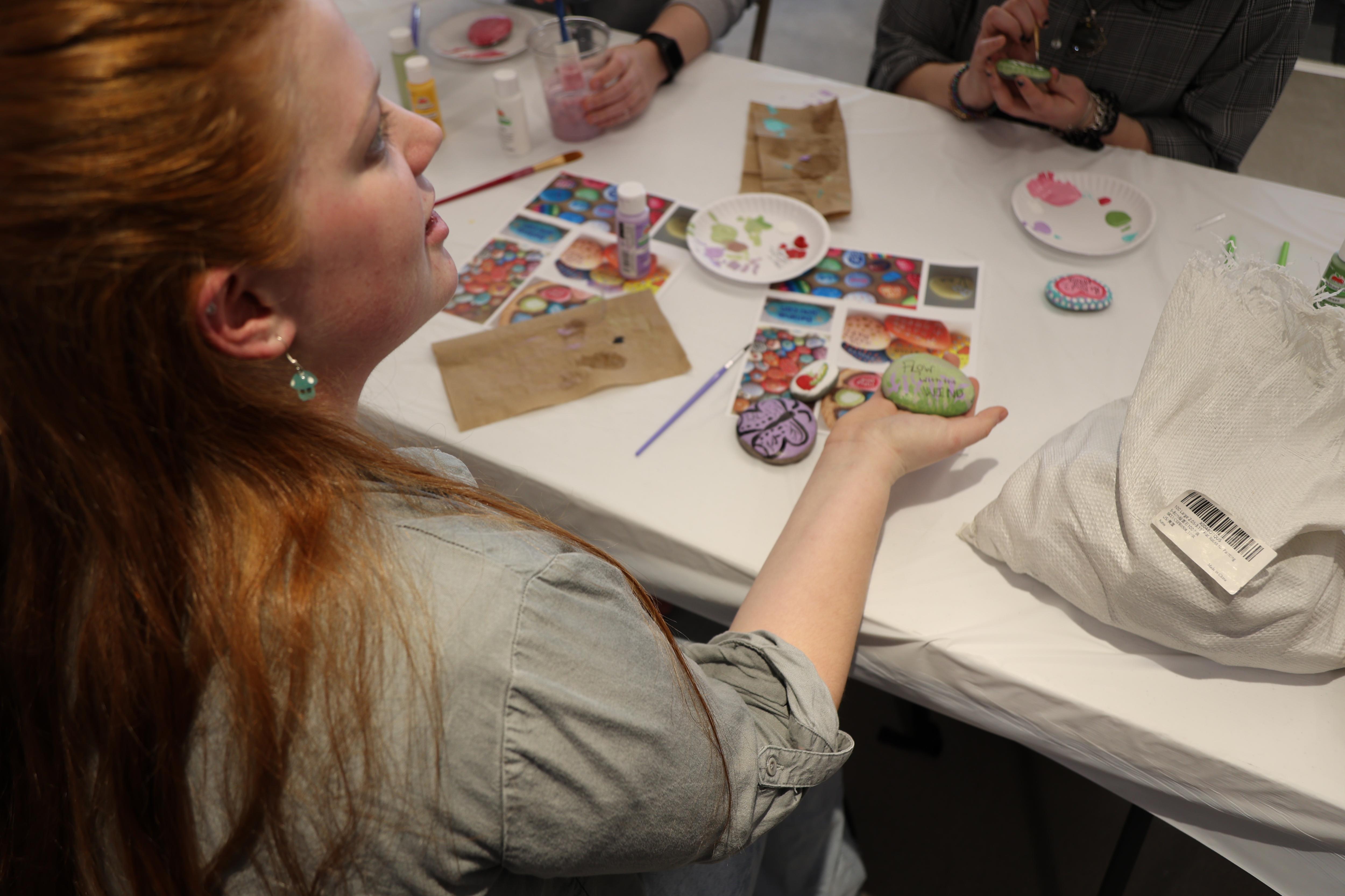 A student at a table holds up a painted kindness rock