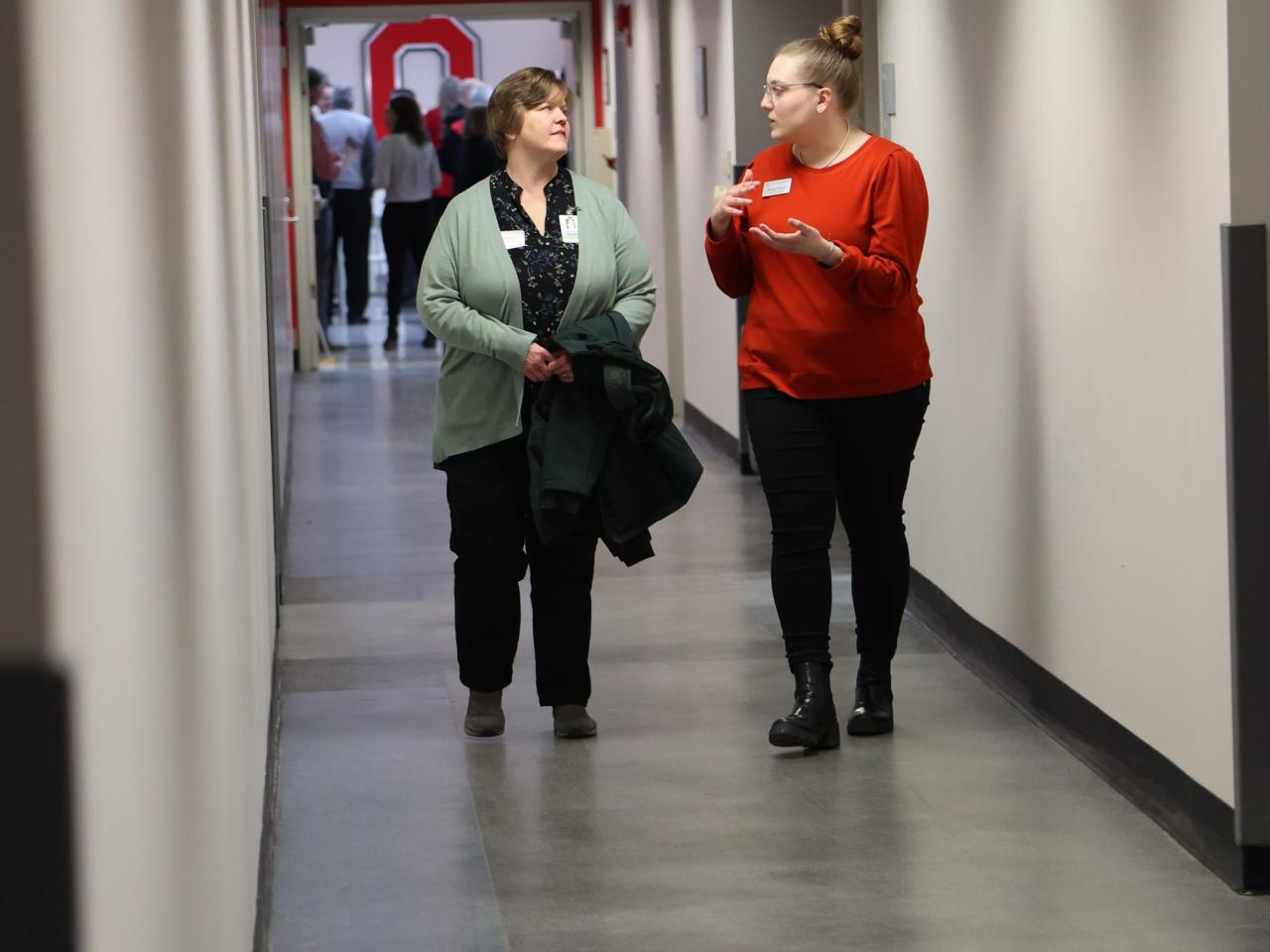 Two women talk as they walk down a hall