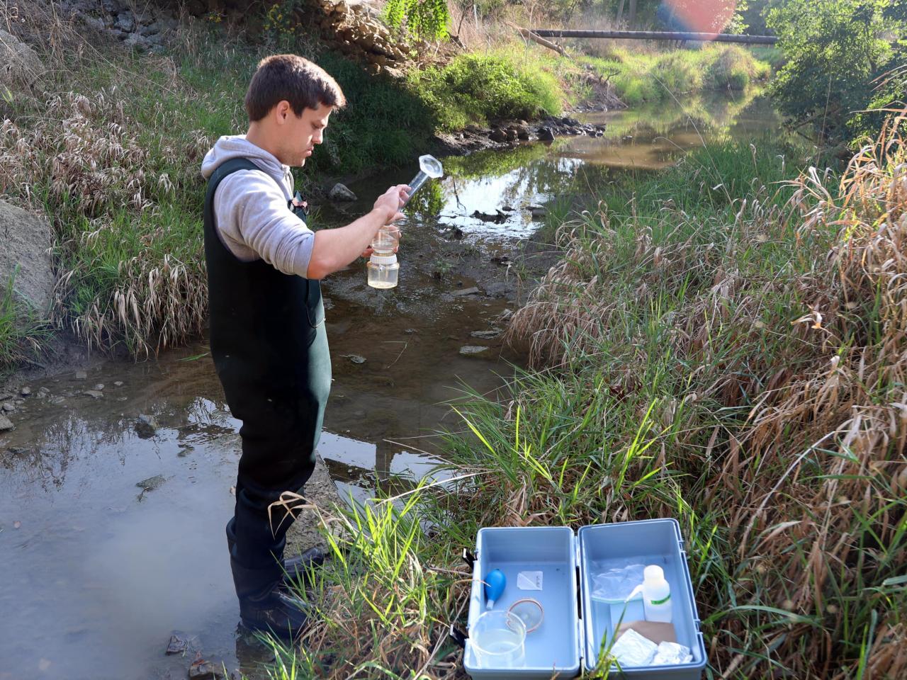 Undergraduate researcher Carter Welch pours water from the Lost Creek into a beaker