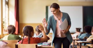 A teacher in a classroom gives a student a high five