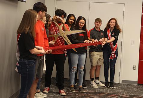 Students in a line cutting a ribbon with large scissors