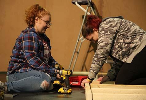 Two students build a wall with power tools.