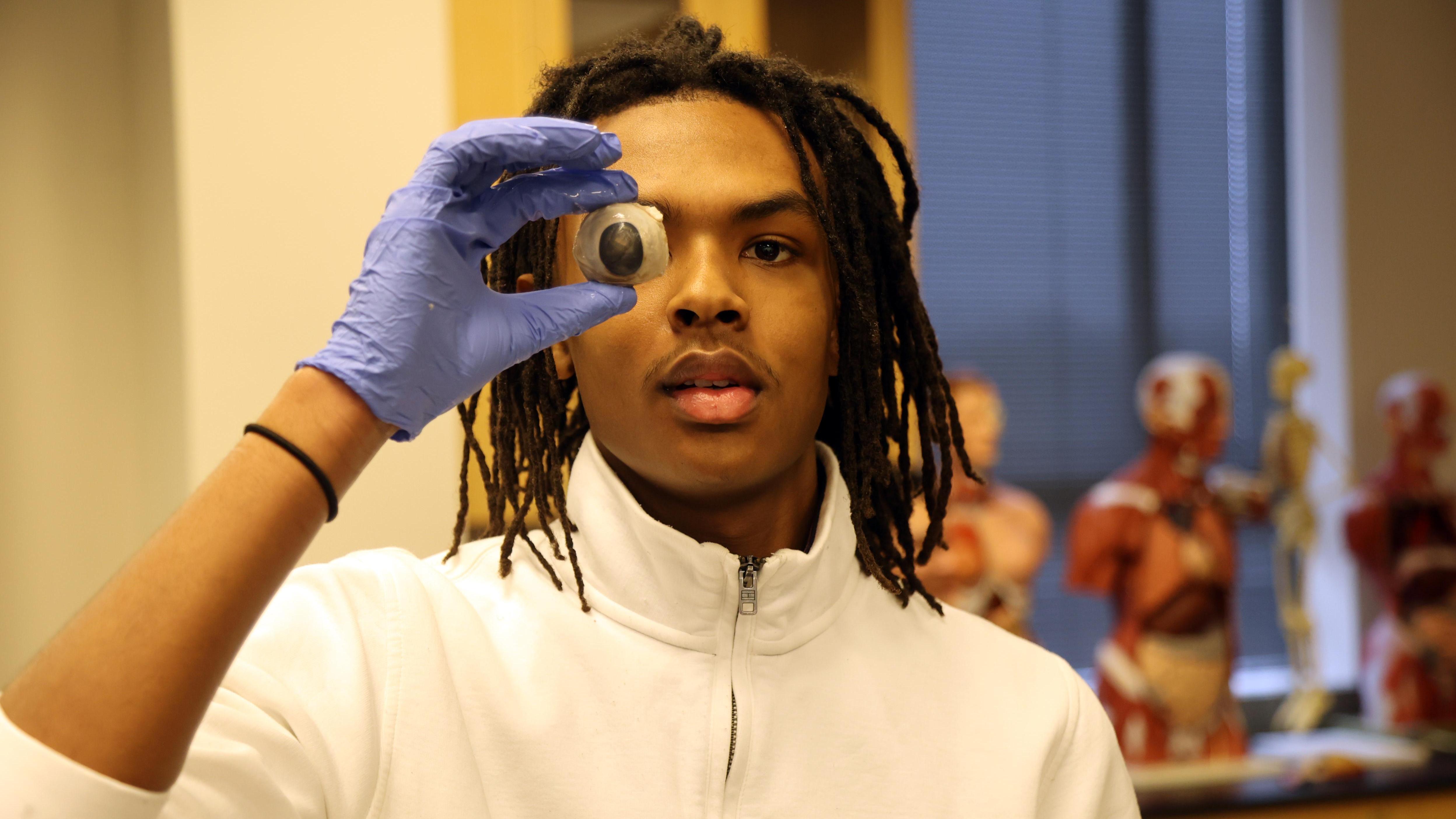 A student holds a cow eye in front of his face