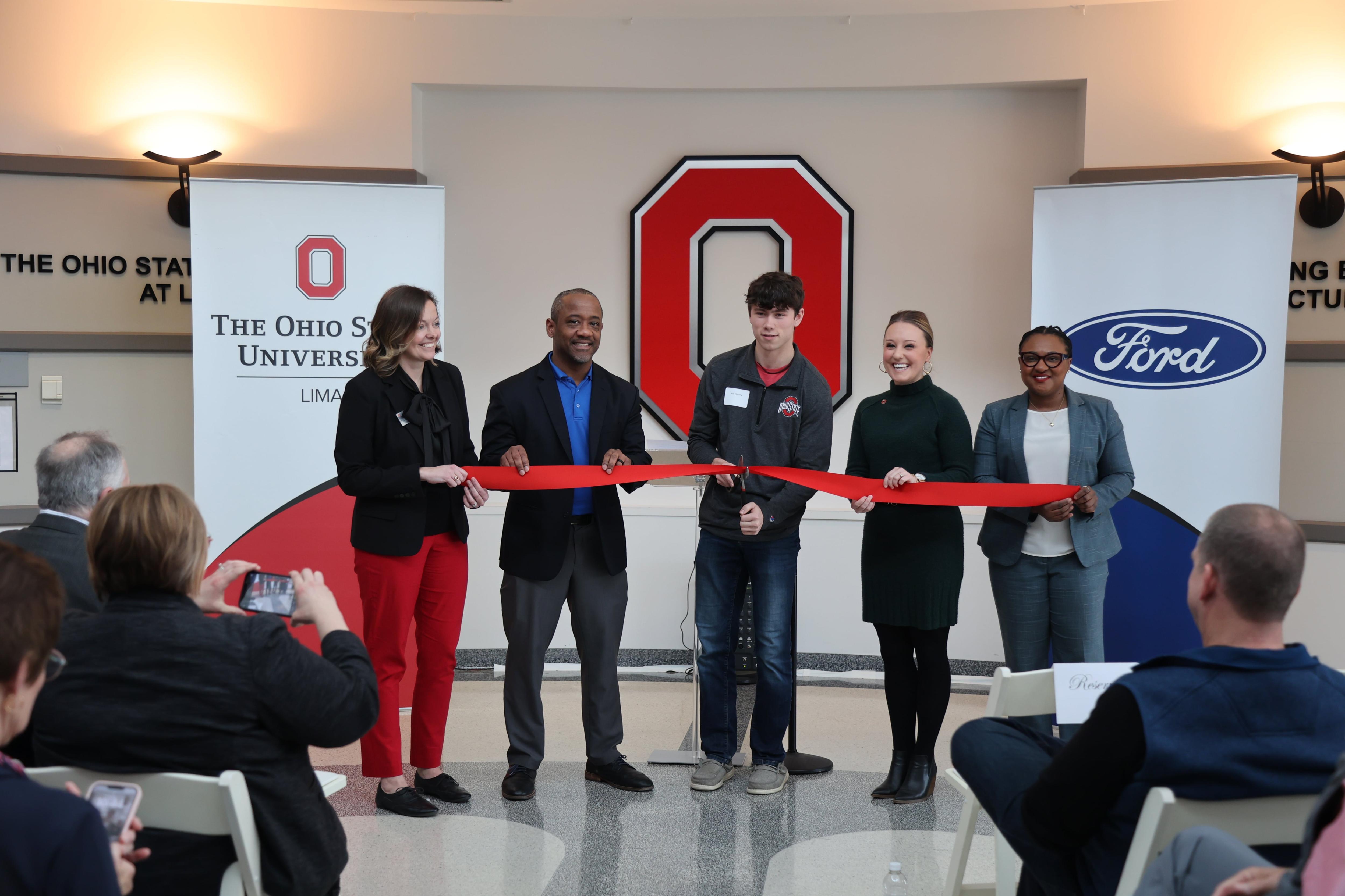 Five people cut a ribbon in front of a Block O 