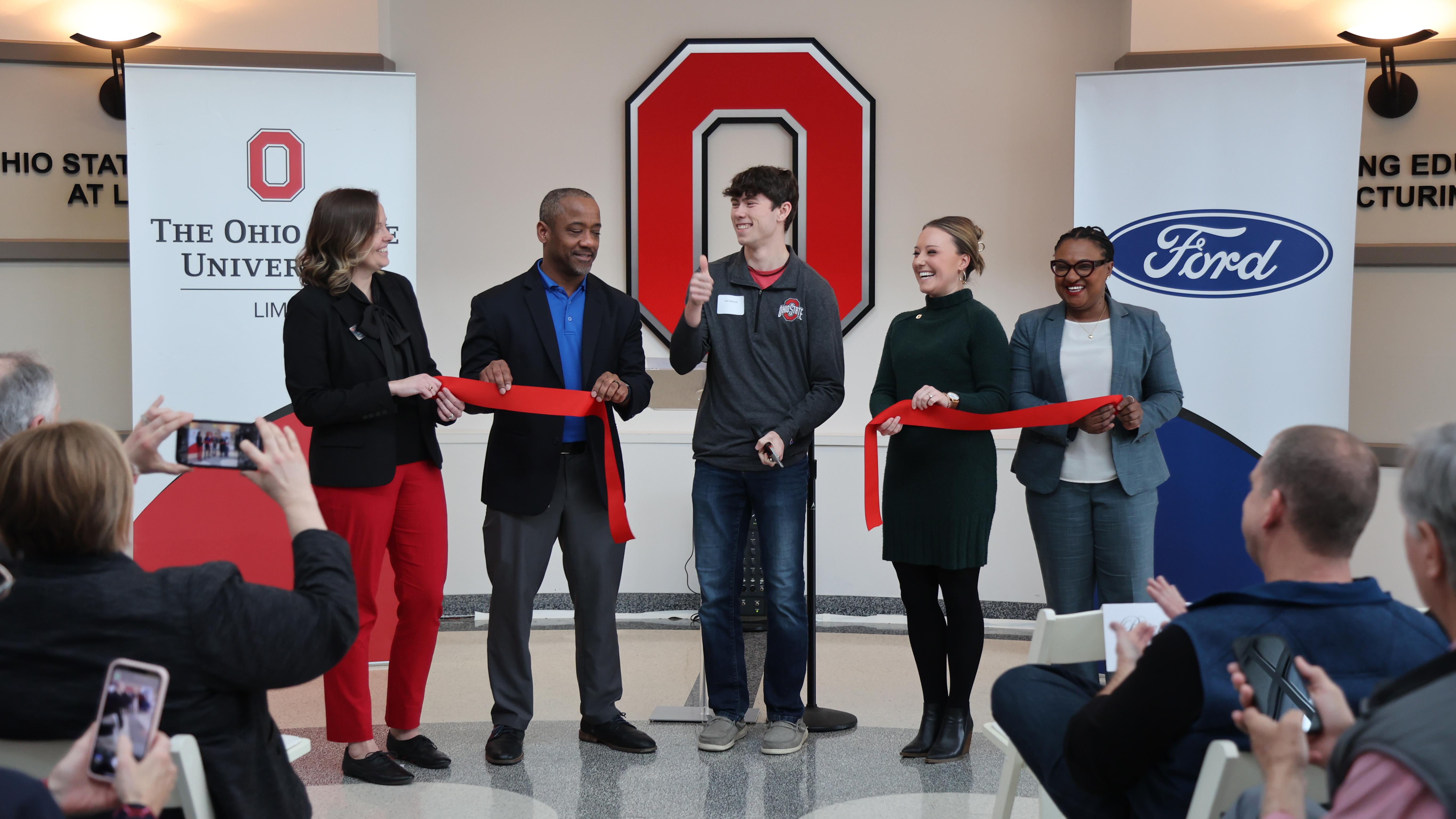 Five people in front of a Block O cut a ribbon at the Engineering Education and Manufacturing Center