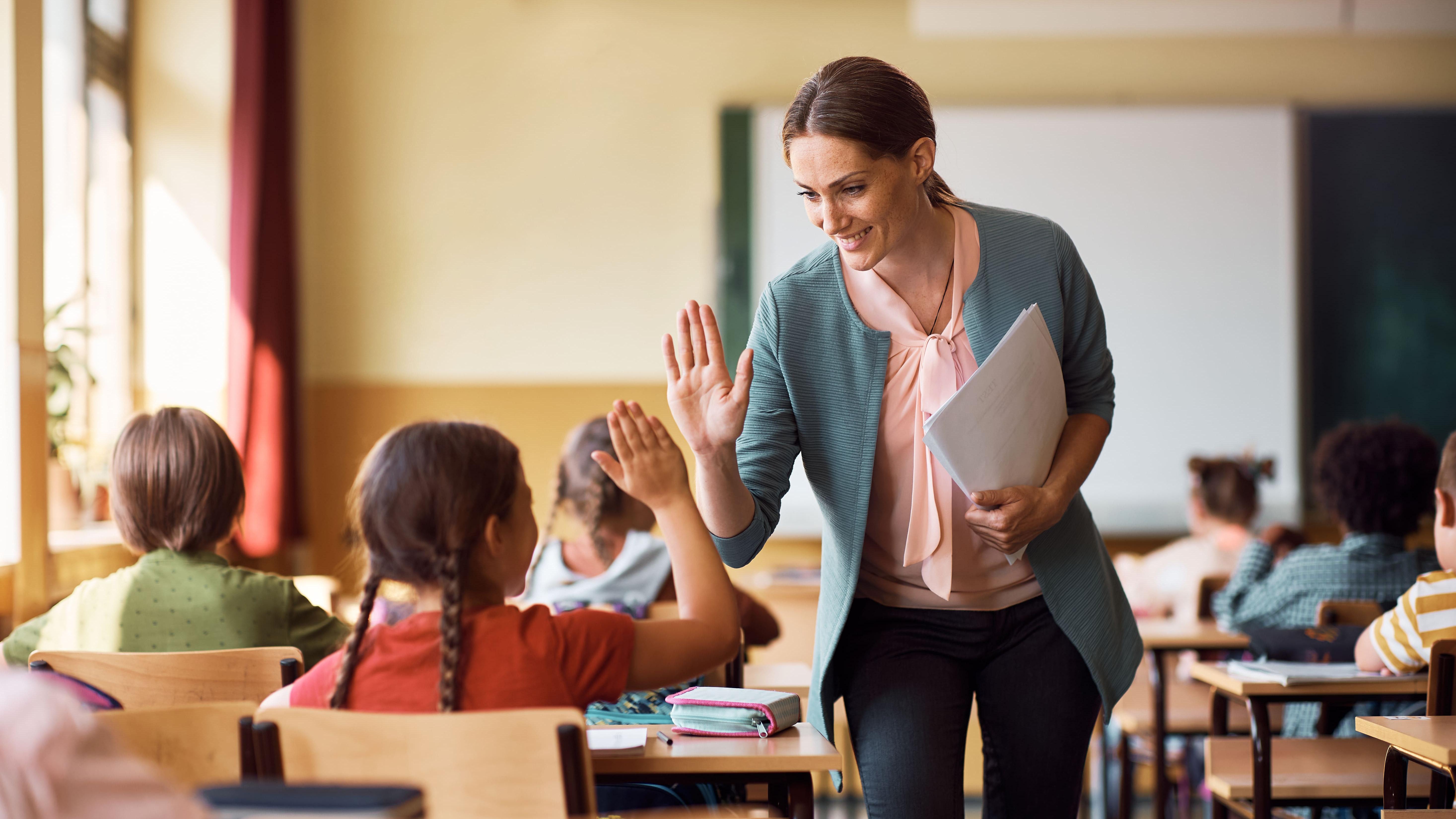 A teacher in a classroom gives a student a high five