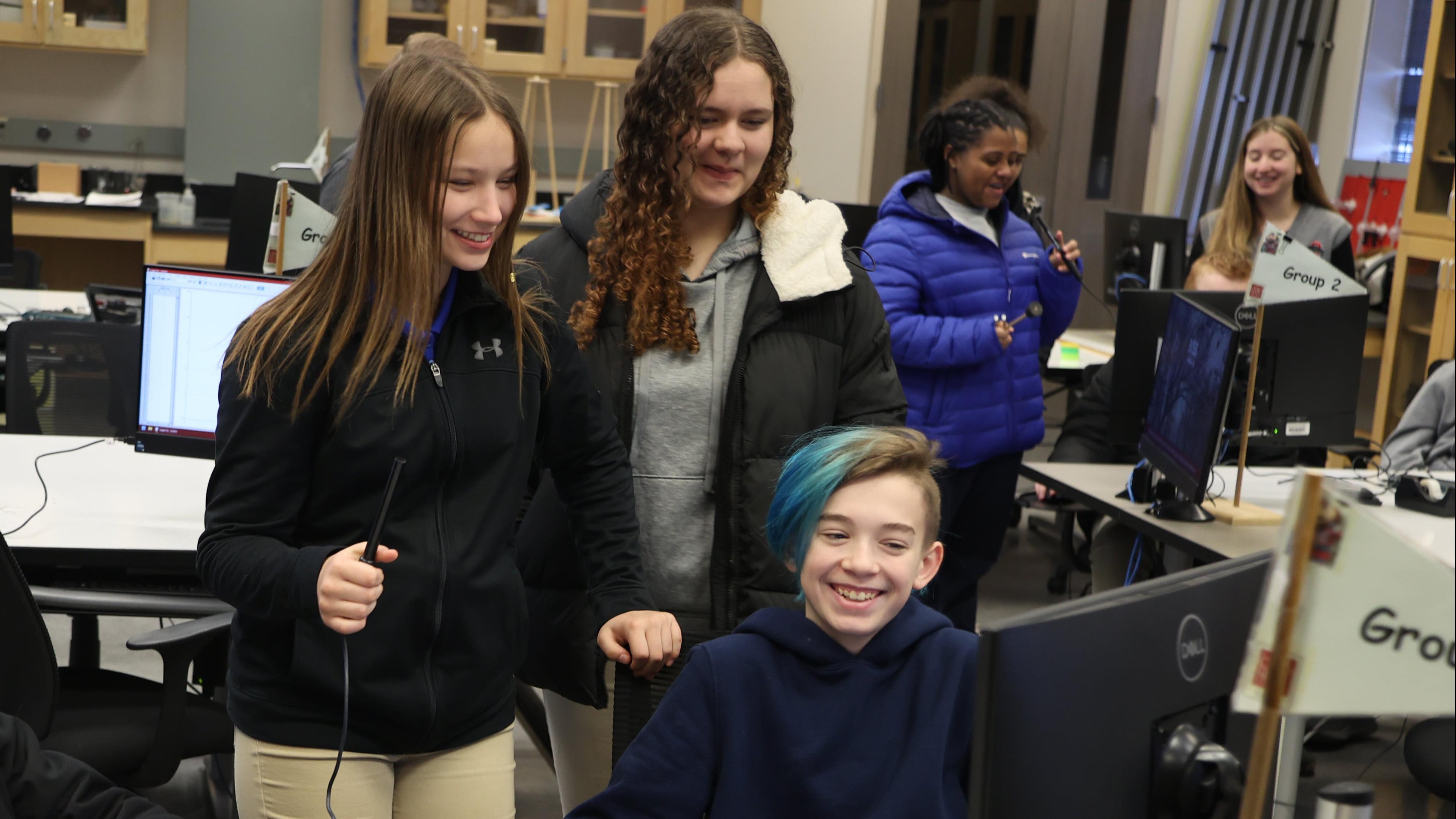 Students laughing around a computer monitor in a science lab