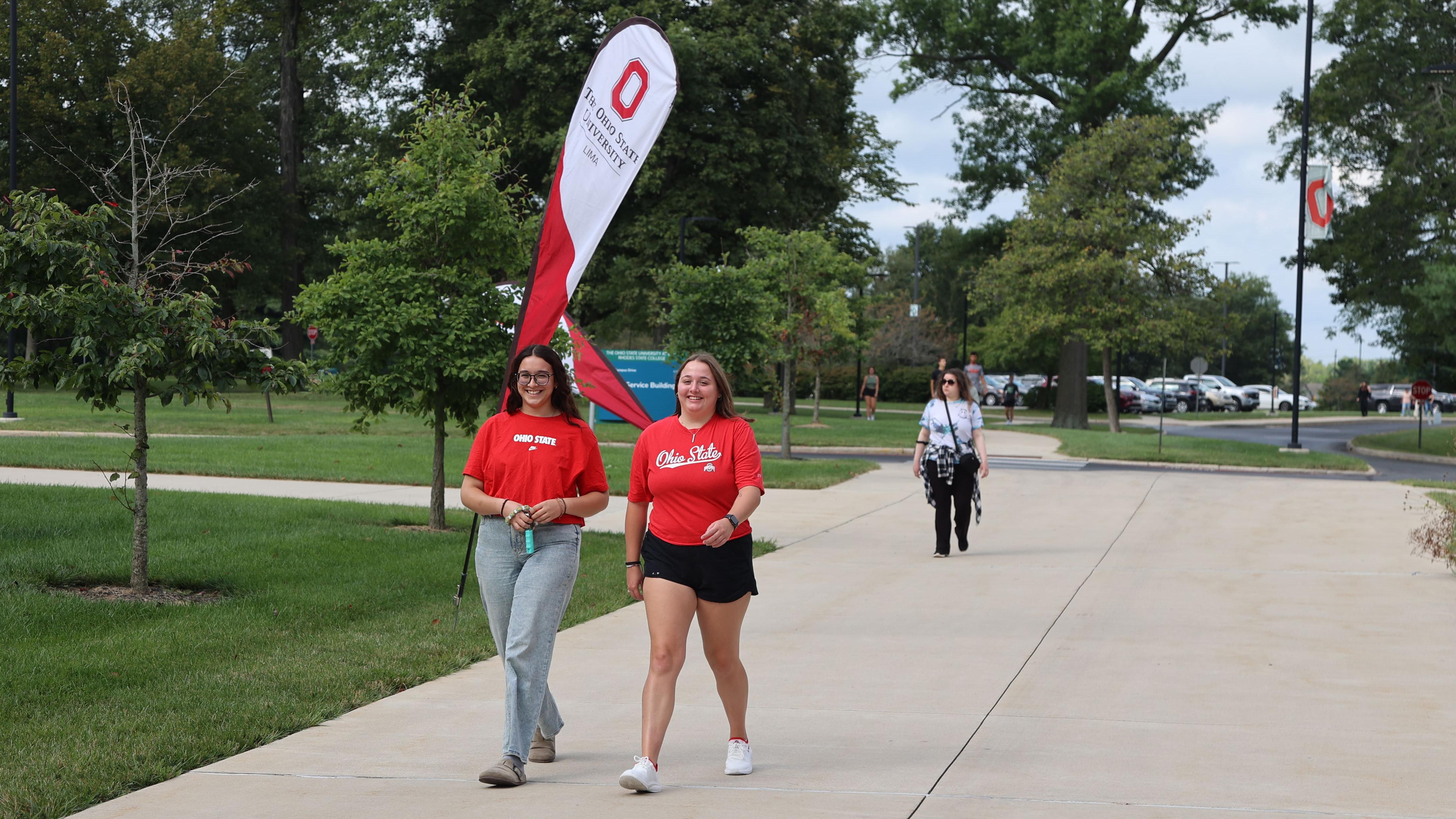 Two students walk in front of an Ohio State Lima flag