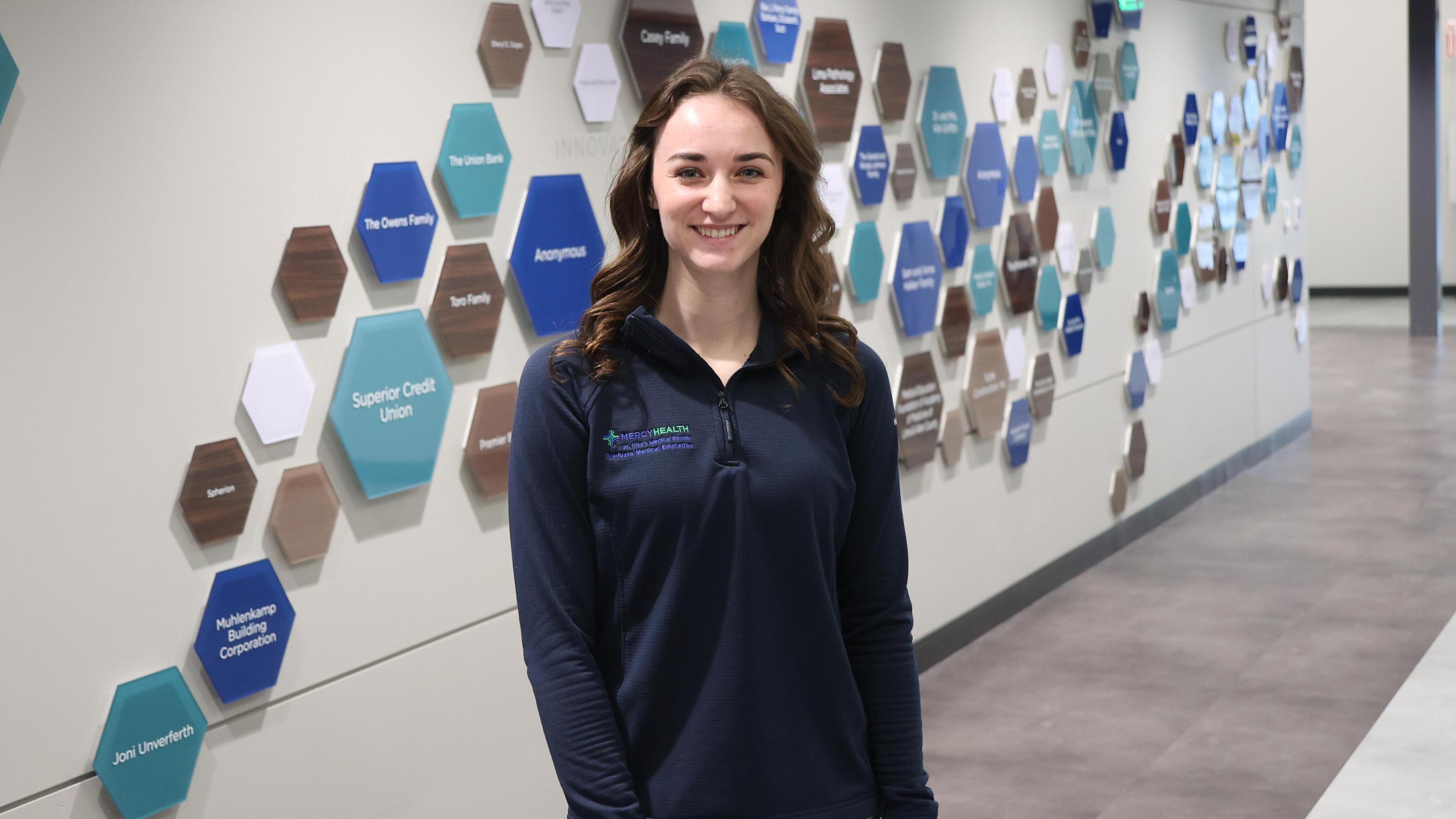 Brooke Kortokrax in front of Mercy's Graduate Medical Center donor wall