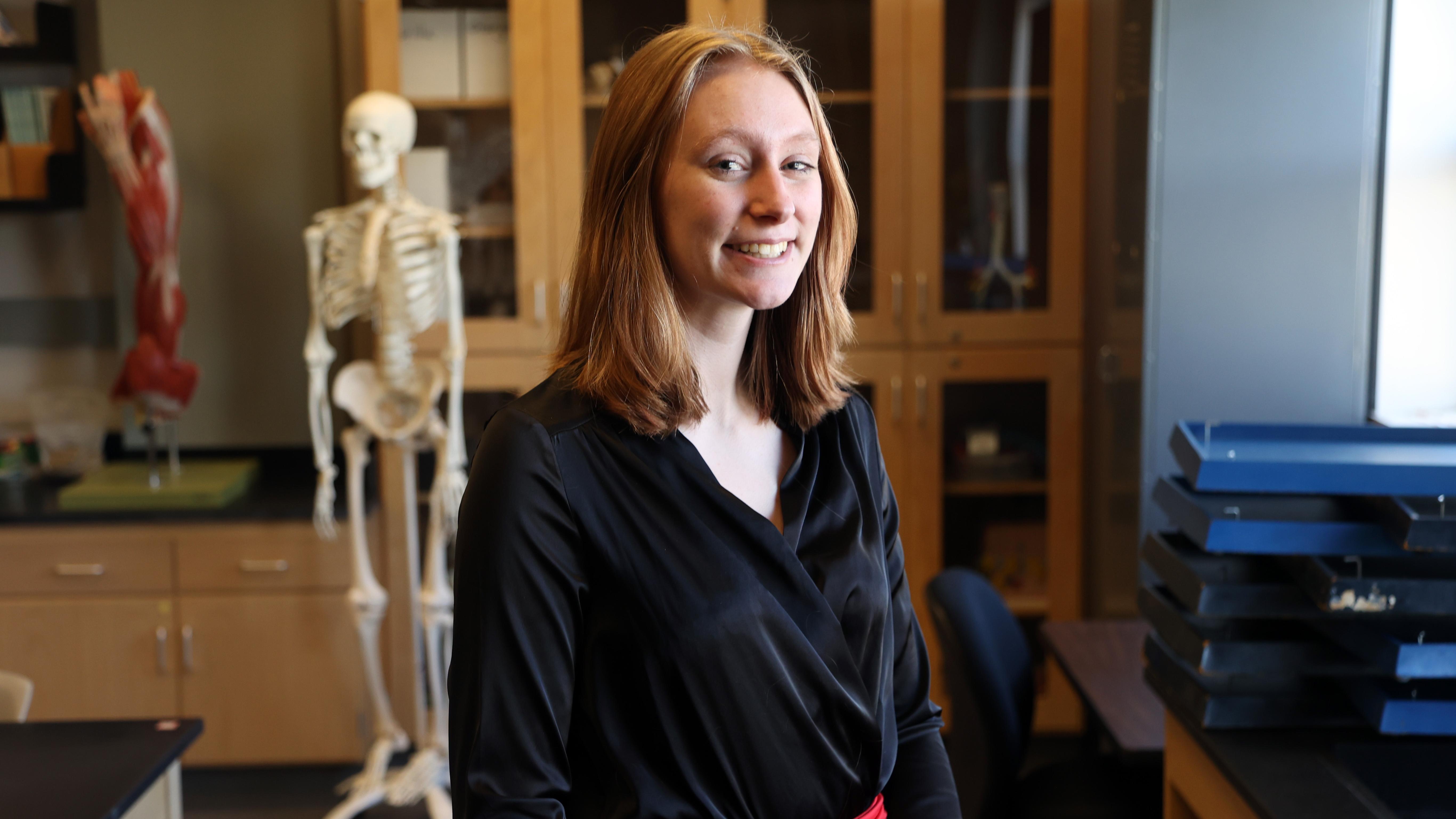 Rachel Ryan in the bio lab next to a skeleton