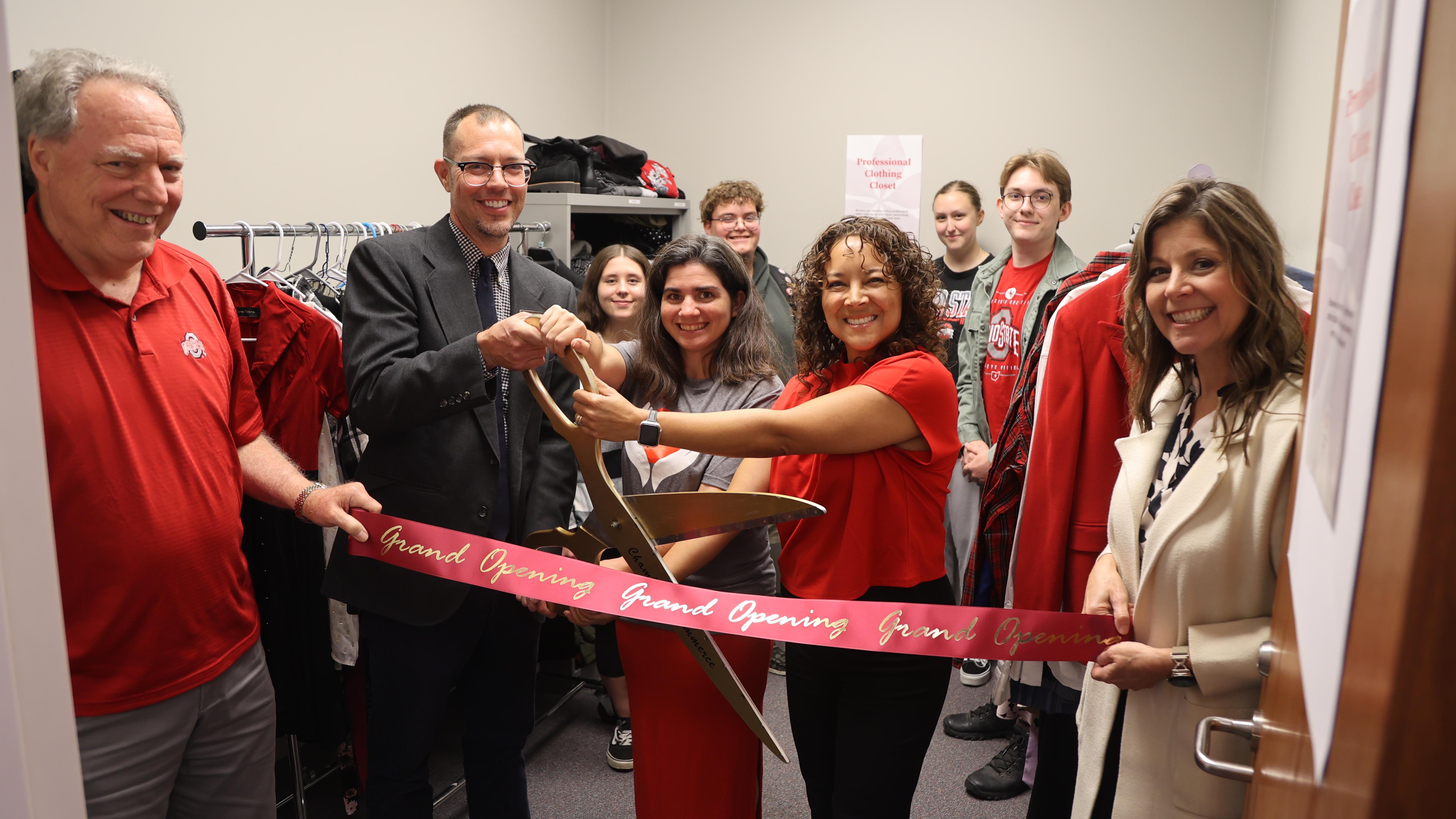 A group holds ribbon and large scissors in a clothing closet