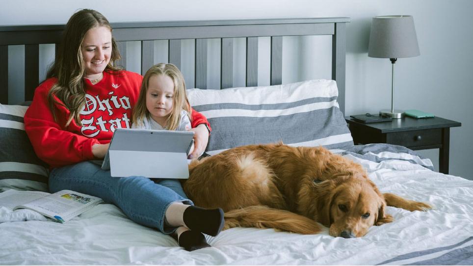 A student and a child look at a tablet next to a dog
