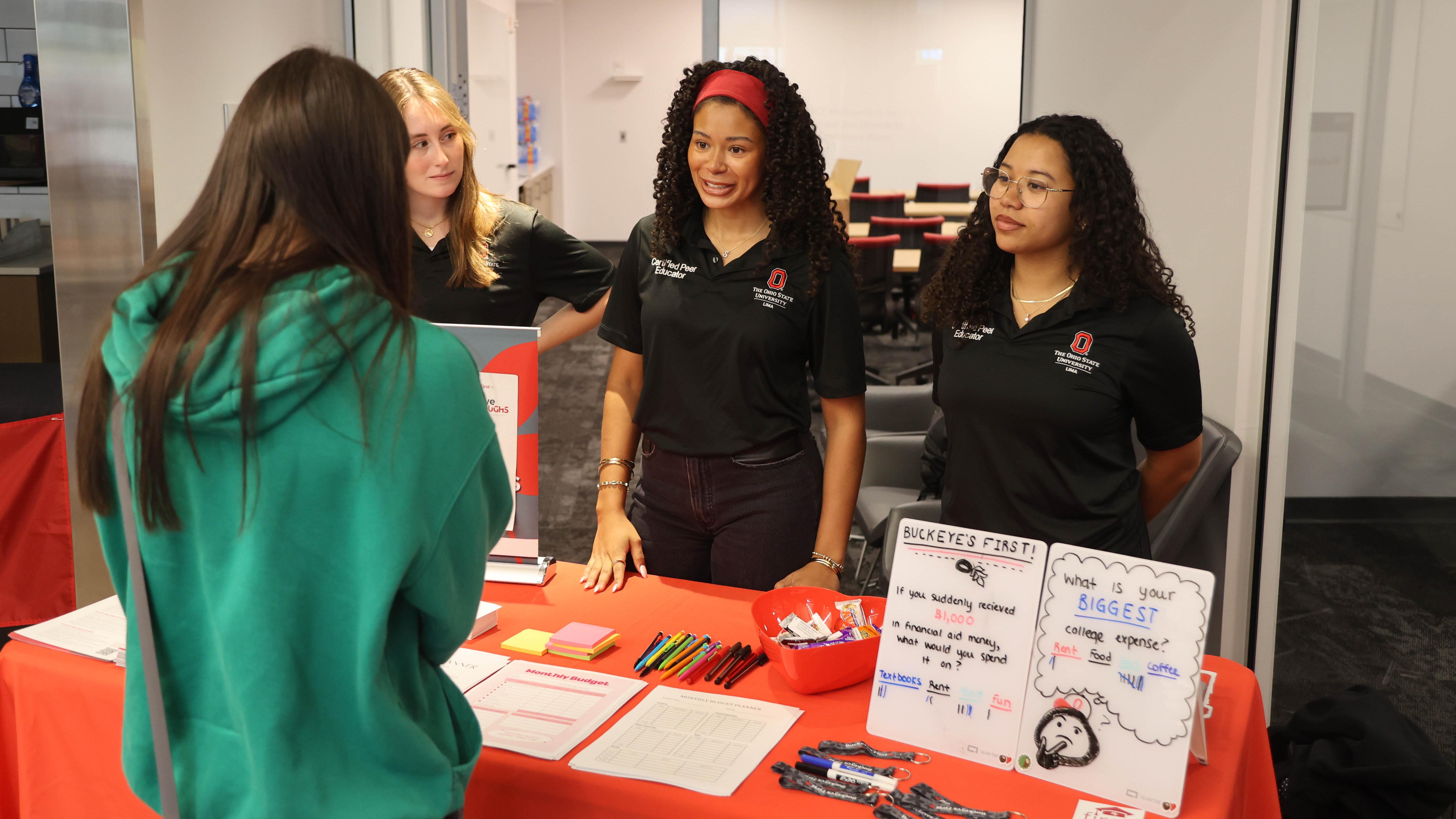 Three students in matching polos talk to another student at a Wellness Fair table