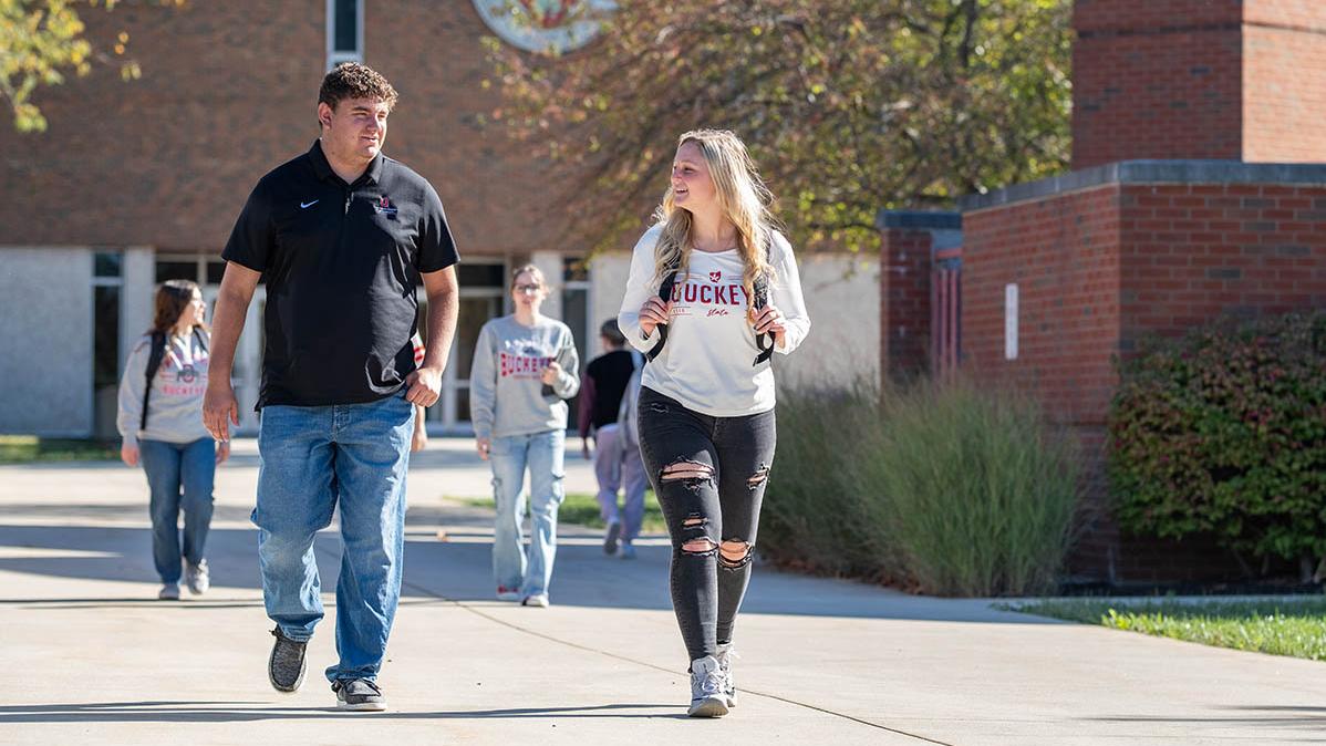 Two students walk on a campus sidewalk with Galvin Hall in the background
