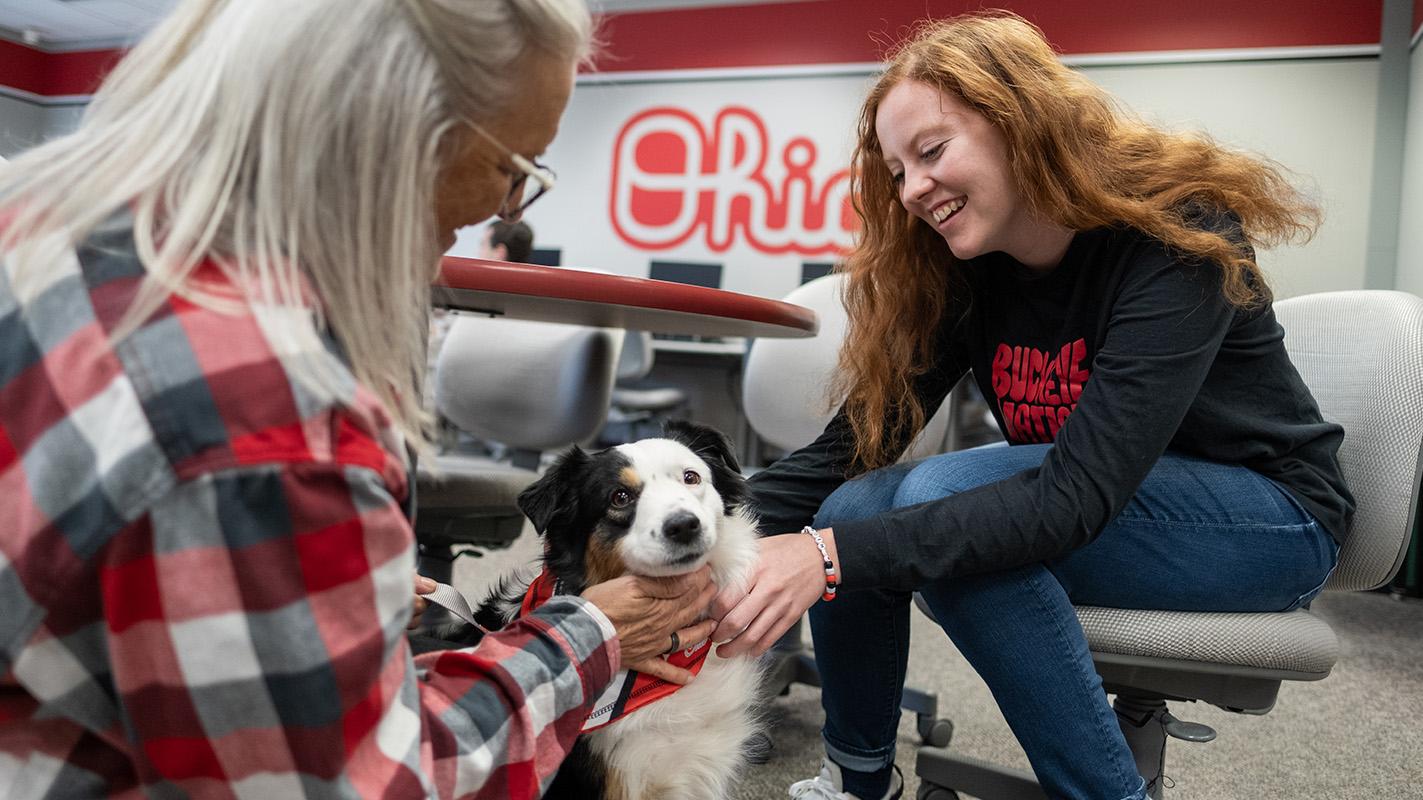 Two people sit on either side of a therapy dog