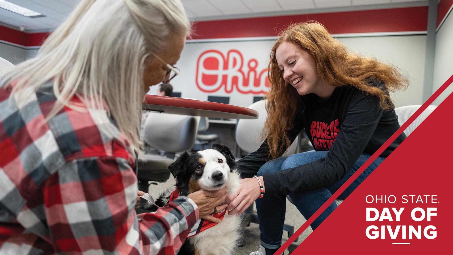 Two people sit on either side of a therapy dog