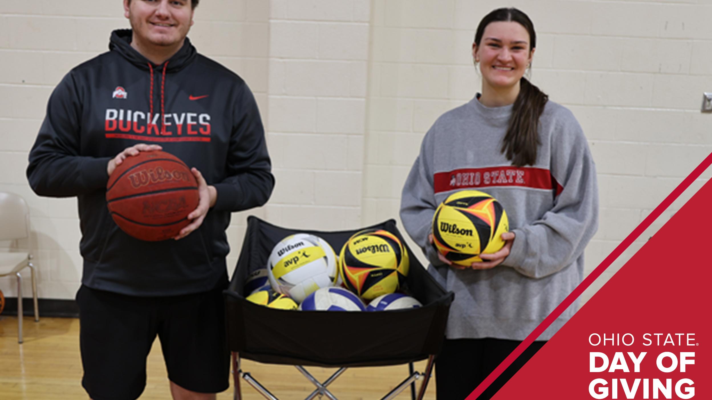 Two students holding basketballs stand near a ball hamper in a gym
