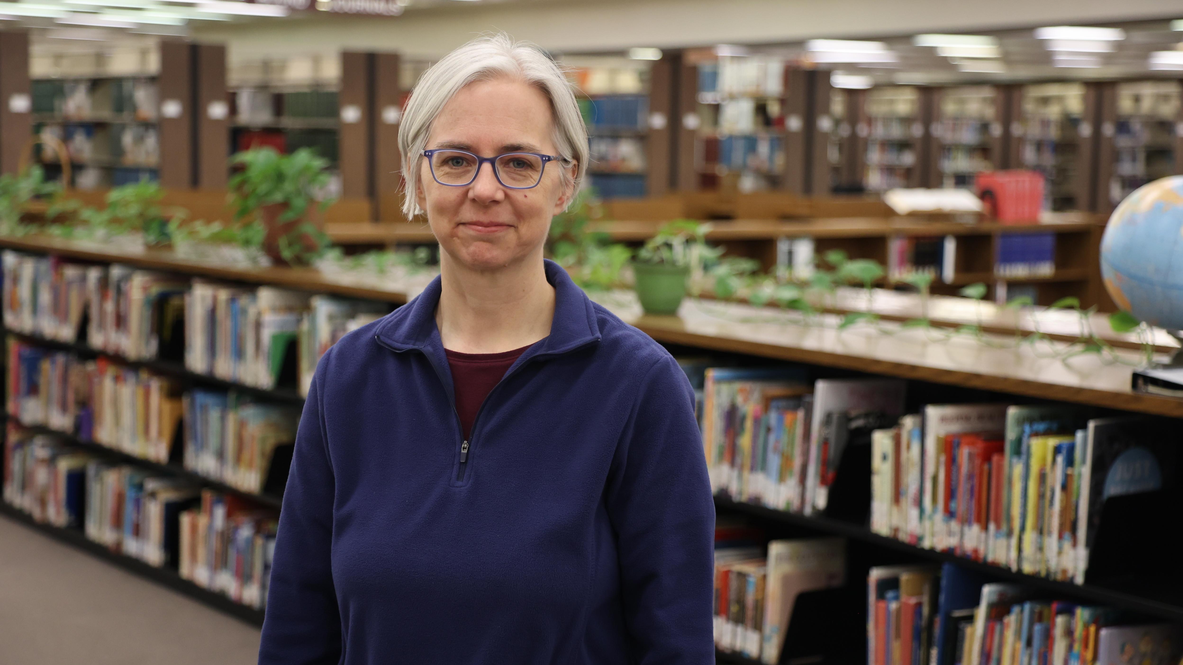 Librarian Tina Schneider stands in front of racks of library books. 
