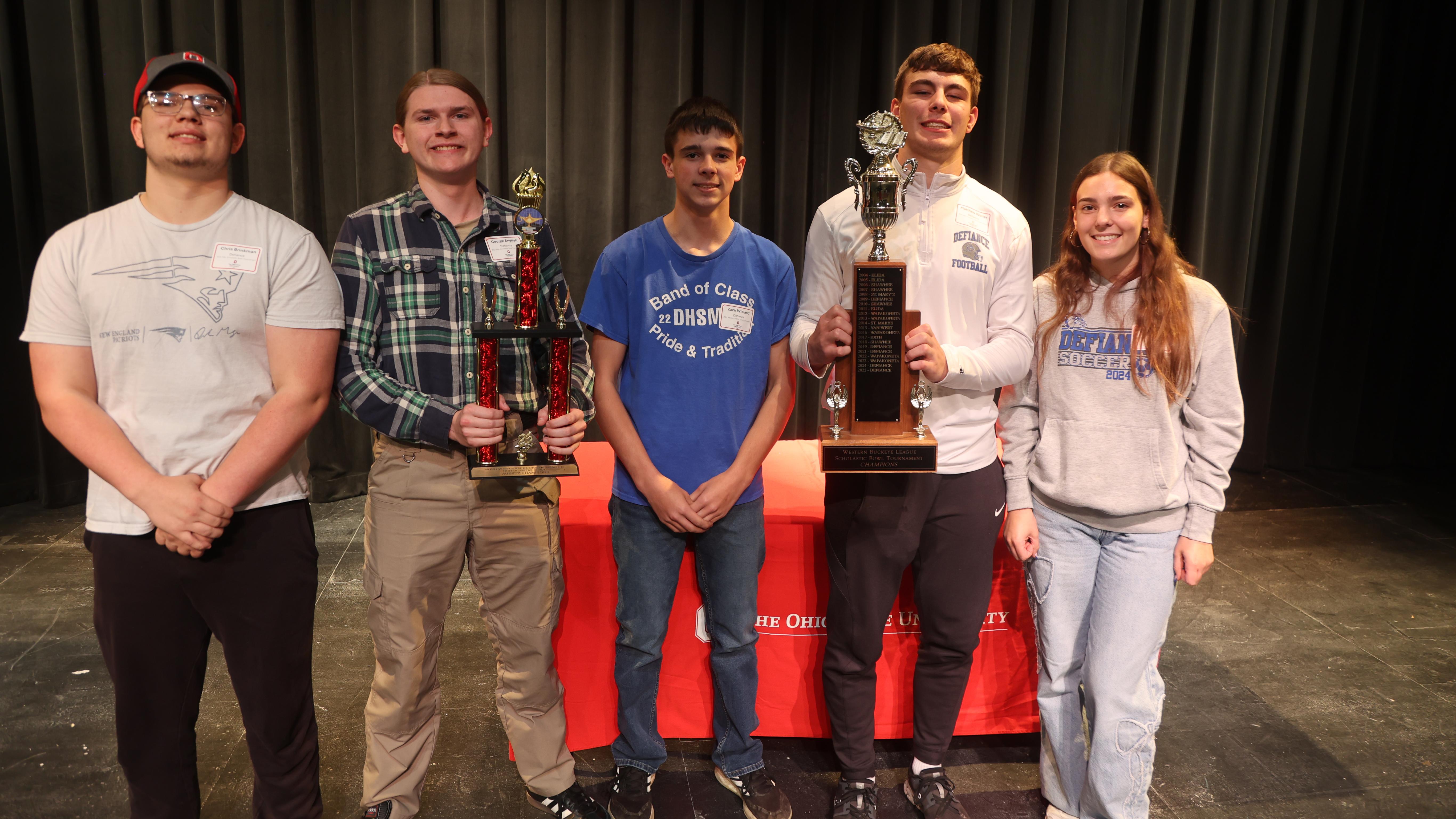 Five scholastic bowl competitors hold two trophies. 