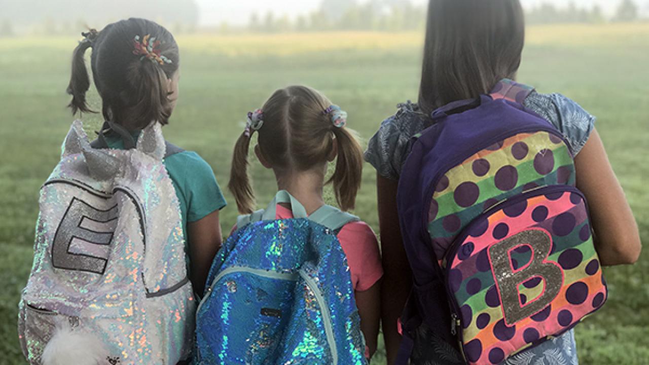 Three young girls facing away wearing backpacks