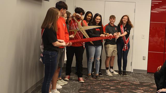 Students in a line cutting a ribbon with large scissors